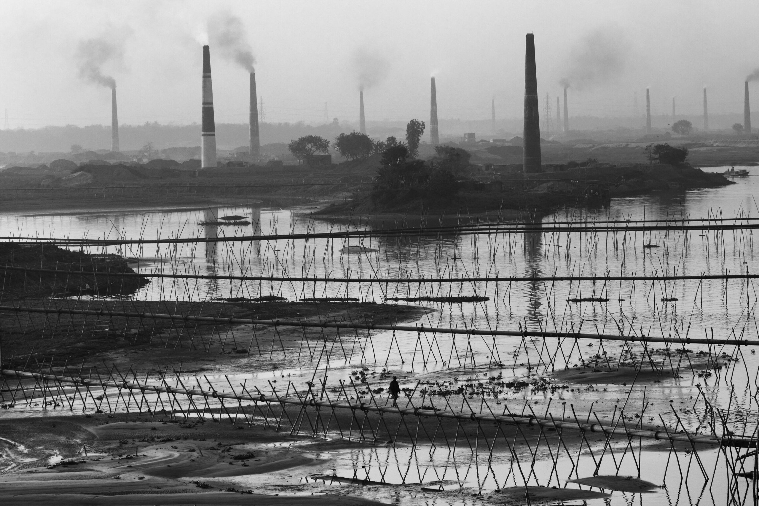 Black and white view of industrial smokestacks in Keraniganj, Bangladesh, reflecting in the river.